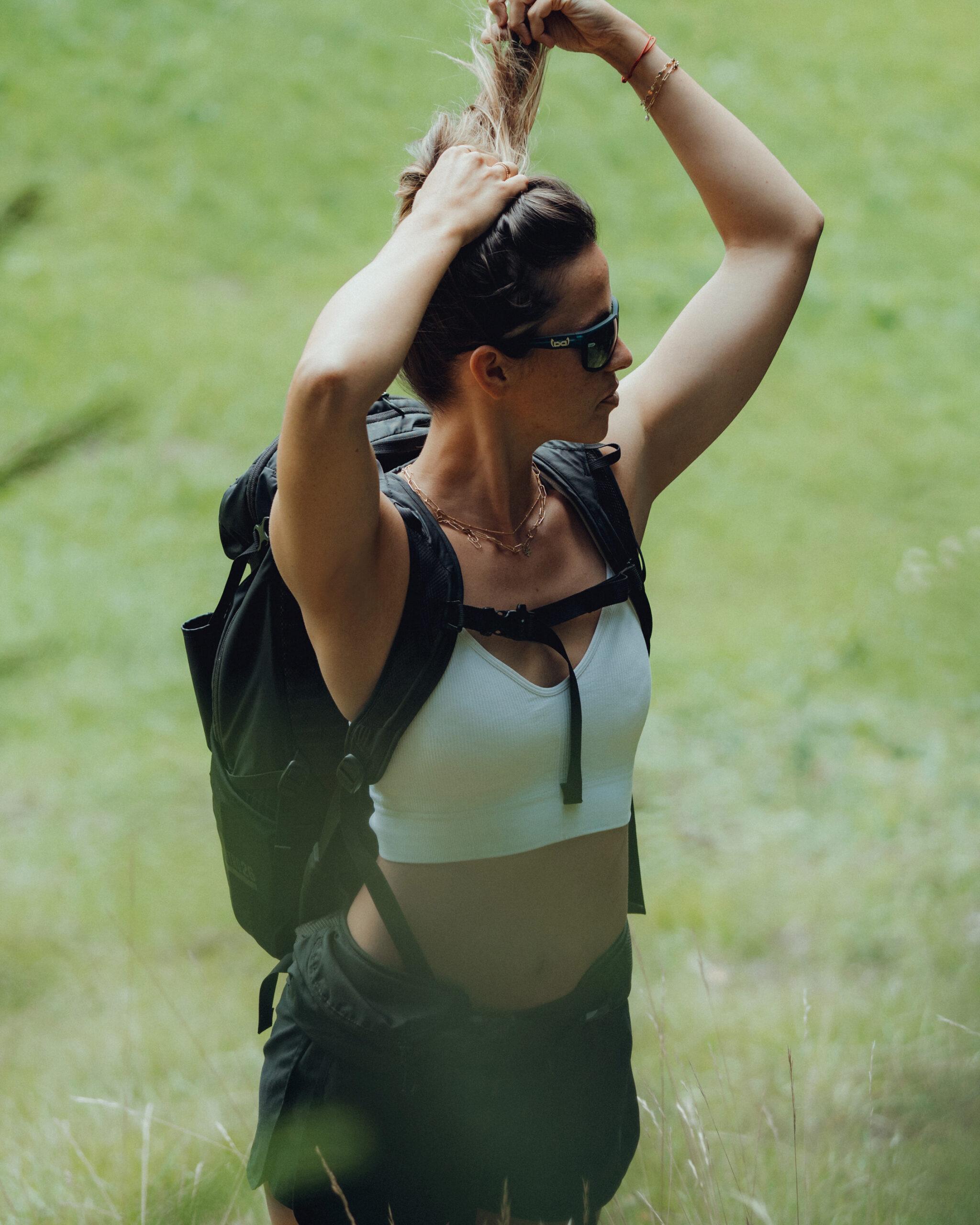 Frau mit gloryfy Sportbrille und Rucksack beim Wandern in gruener Landschaft