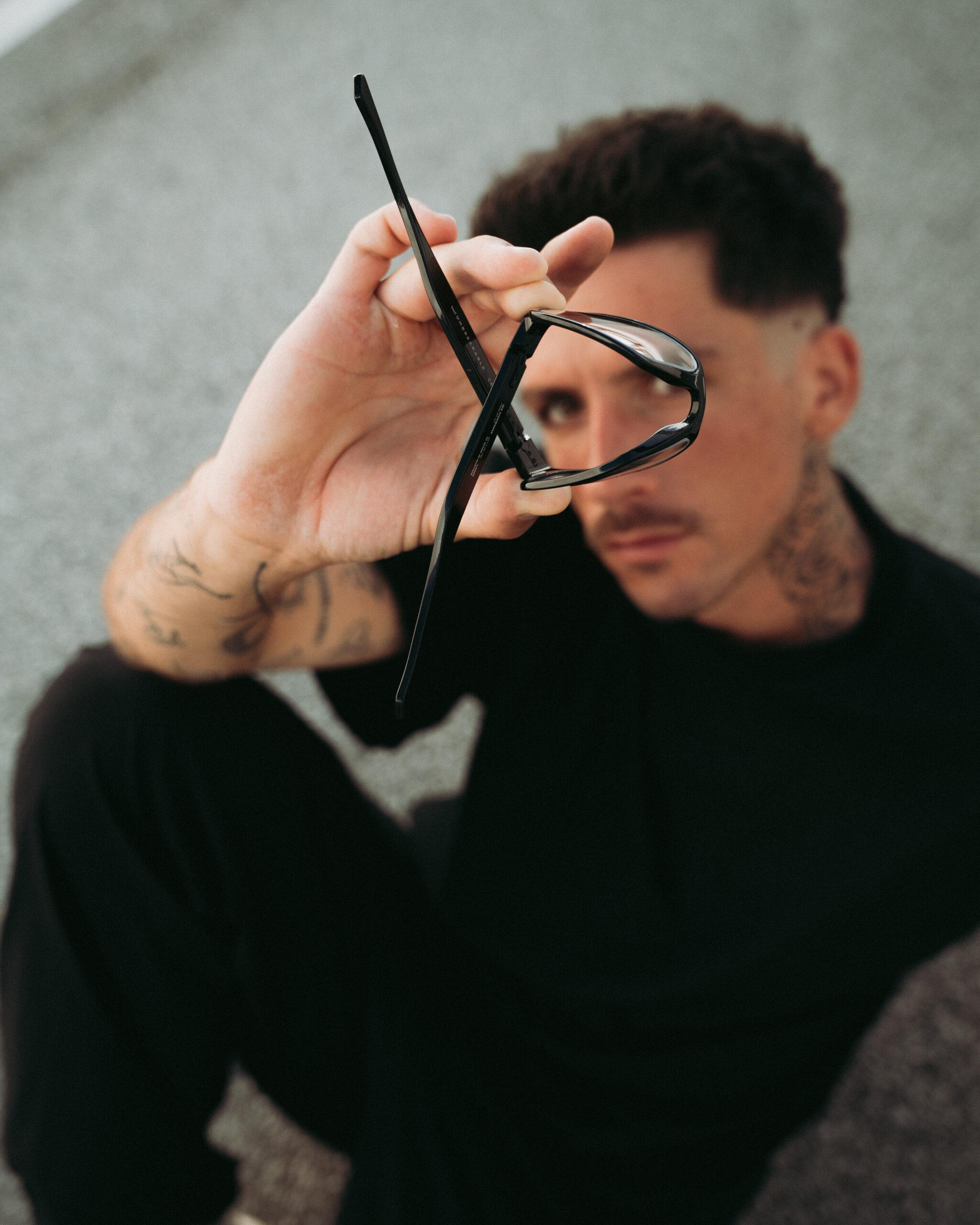Mann haelt eine gloryfy unbreakable Sonnenbrille pruefend in der Hand, Nahaufnahme des Rahmens